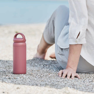 Person sitting on a sandy beach with a pink water bottle nearby