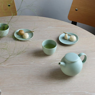 Light green teapot with cups and plates with snacks on a table