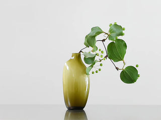 Green vase with a branch of leaves on a light gray background
