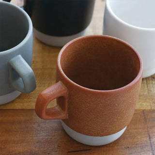 Orange ceramic mug on a wooden surface with other mugs in the background