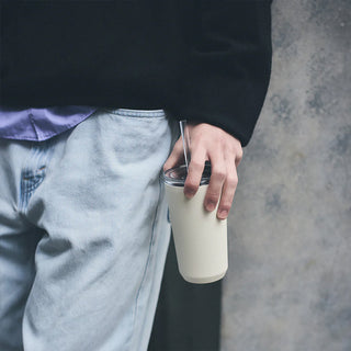 Person holding a white tumbler with a straw against a gray background