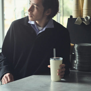Man sitting at a table holding a cup with a straw in a cafe setting