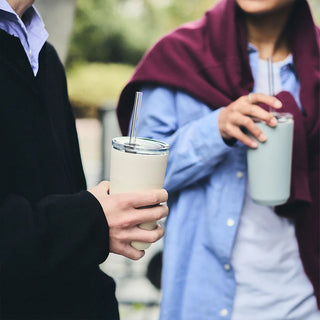 Two people holding insulated cups with straws outdoors