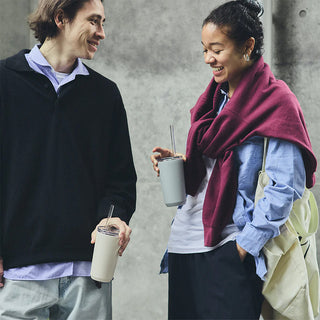 Two people standing close together, each holding a drink with straws against a concrete wall.