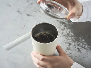 Person holding lid over a white cup on a gray surface