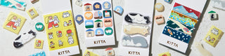 Different KITTA washi tapes open and small stickers on a concrete surface