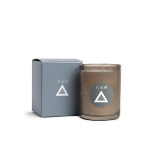 Candle with 'ASH' logo next to its packaging on a white background