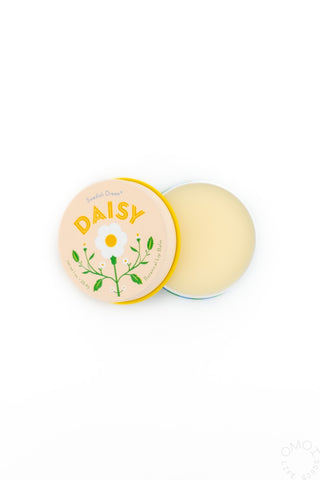 Opened container of Kala Skandi Daisy Lip Balm with yellow packaging and a daisy on a white background
