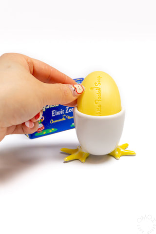 Hand holding yellow soap on a white ceramic egg cup on a white background