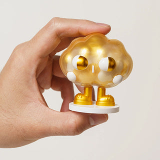 Hand holding a small golden cloud-shaped figurine with white accents on a plain background