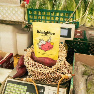Yellow package of 'KinglyParc' on a woven bag with sweet potatoes in a market setting