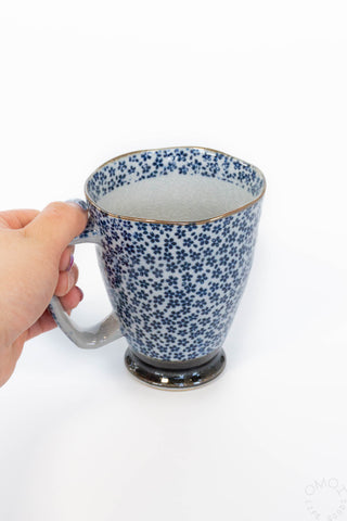 Hand holding a blue and white patterned mug on a white background