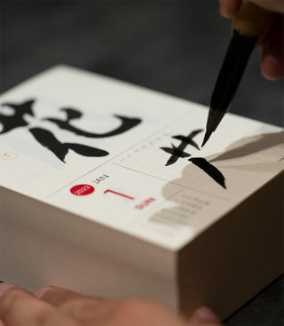 Person writing calligraphy on a white surface with a brush