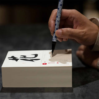 Hand holding a calligraphy pen over a calendar on a dark background