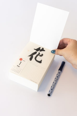 Hand holding a pen over a calendar with Japanese characters on a white background