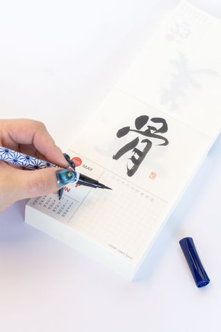 Hand holding a brush pen with calligraphy on a white background
