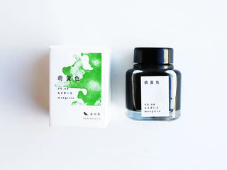 A bottle of ink next to its white packaging box, features a green ink splash design