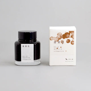 A bottle of ink and its white packaging. The bottle has a black cap and a white label with Japanese text, and the box features brown ink splatter graphics