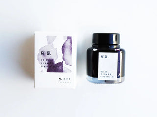 A bottle of ink and its matching box on a plain white background with a purple watercolor design and black text