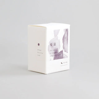 bottled ink packaging with minimalist purple watercolor-style ink splatter and small text, on a light background.