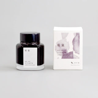Ink bottle and packaging with purple ink splatter design on a light gray background