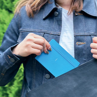 Person holding a blue notebook with a blurred green background