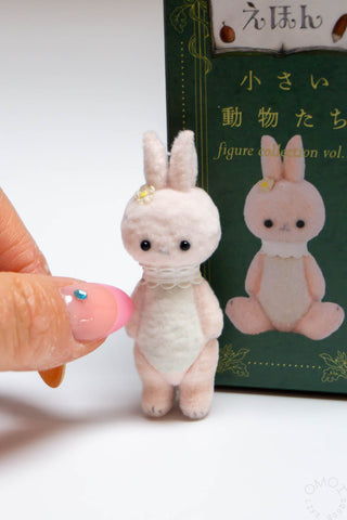 Small plush rabbit toy held by a hand with a book about figurines in the background.