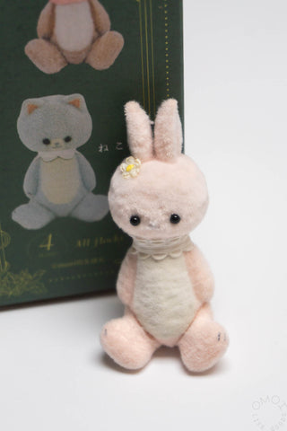 Plush rabbit toy with a decorative bow in front of a green box with illustrations.