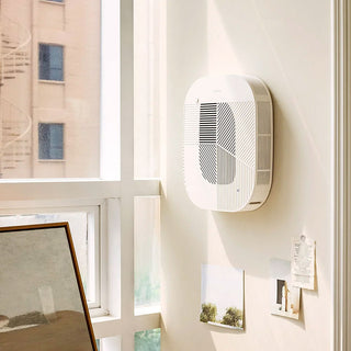 Cream white air purifier mounted on a wall near windows and notes