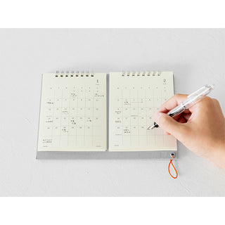 Hand holding a pen over an open spiral-bound calendar on a white surface