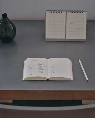 page a day planner on a table with handwriting in it sitting on a desk. in the background is a desk calendar and a vase