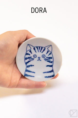 Hand holding a small white ceramic plate with a blue cat illustration on a white background