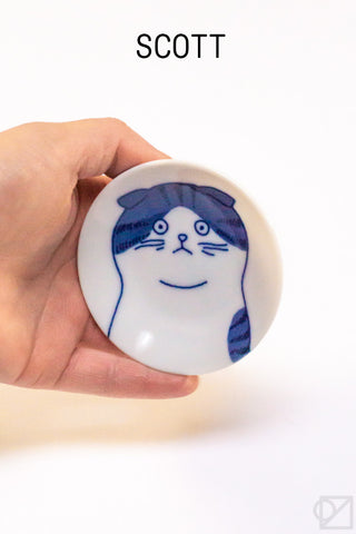 Small white dish with a blue cat illustration held by a hand on a white background