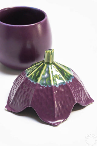 Purple ceramic eggplant shaped jar with green top on a white background