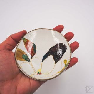 Hand holding a small ceramic dish with flower design on a white background