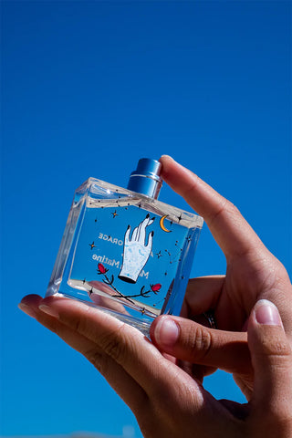 Hand holding a clear perfume bottle with artistic design against a blue sky