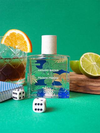 Perfume bottle with decorative label on a green background with a cocktail and dice.