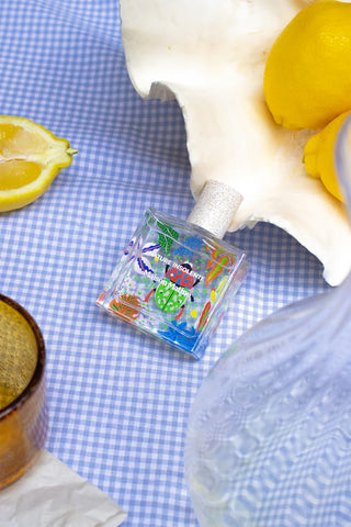 Small glass bottle with colorful design on a blue checkered tablecloth with lemons and a shell.