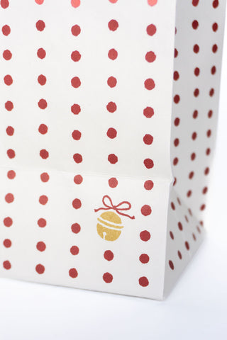White gift bag with red polka dots and a gold bell logo on a white background