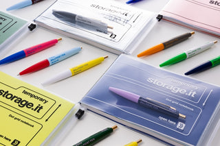 Colorful markers and notebooks with 'temporary storage.it' branding on a white surface.