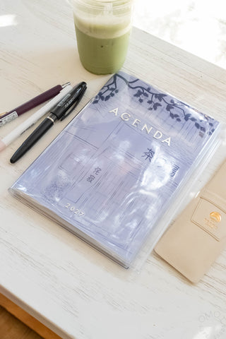 planner with blue cover on a table with stationery items and an iced drink 