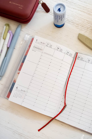 Opened planner showing vertical hourly layout with ribbon bookmarks and stationery items on table