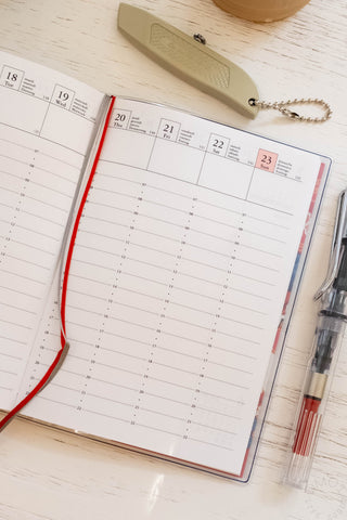 Opened planner showing vertical hourly layout with ribbon bookmarks and stationery items on table