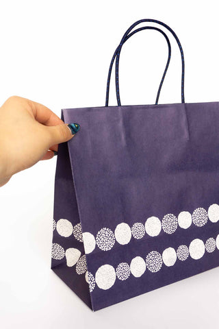 Navy paper bag with white circular pattern held by a hand on a white background