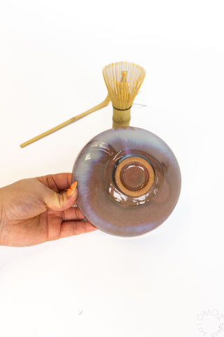 Hand holding a glass bowl with wooden whisk on a white background