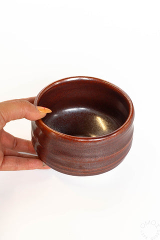 Brown ceramic bowl held by a hand on a white background