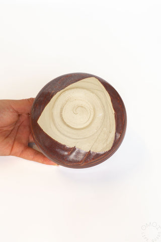 Hand holding a matcha chawan, showing the bottom with a spiral design on a white background