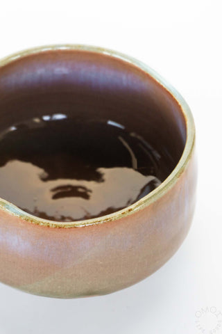 Ceramic bowl with pinkish brownish glaze on a white background