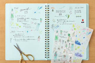 Open notebook with decorative stickers and a pair of scissors on a wooden surface