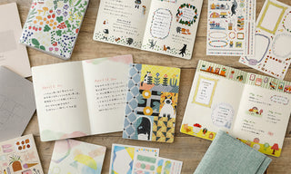 Collection of colorful stationery items including notebooks and sticker sheets on a wooden surface.